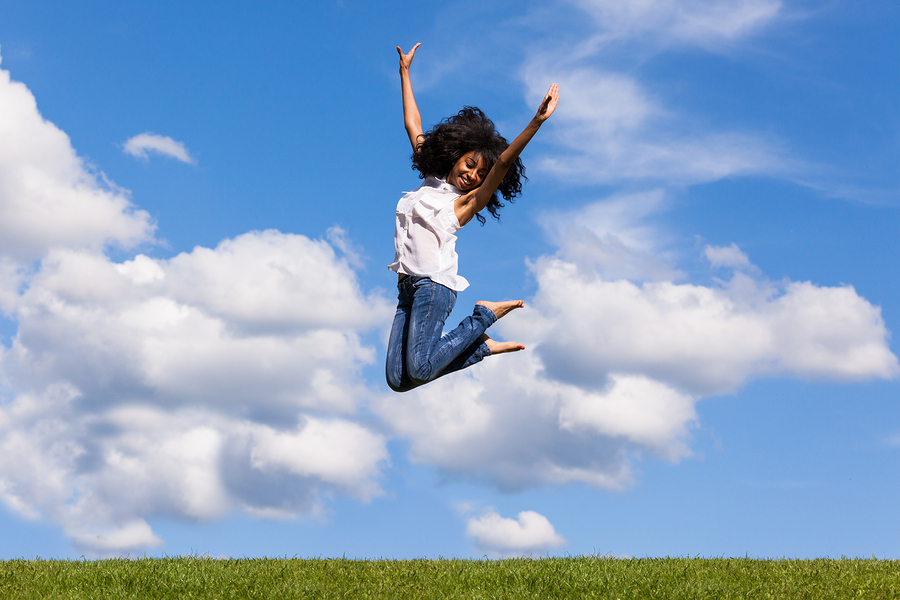 Outdoor Portrait Of A Teenage Black Girl Jumping Over A Blue Sky