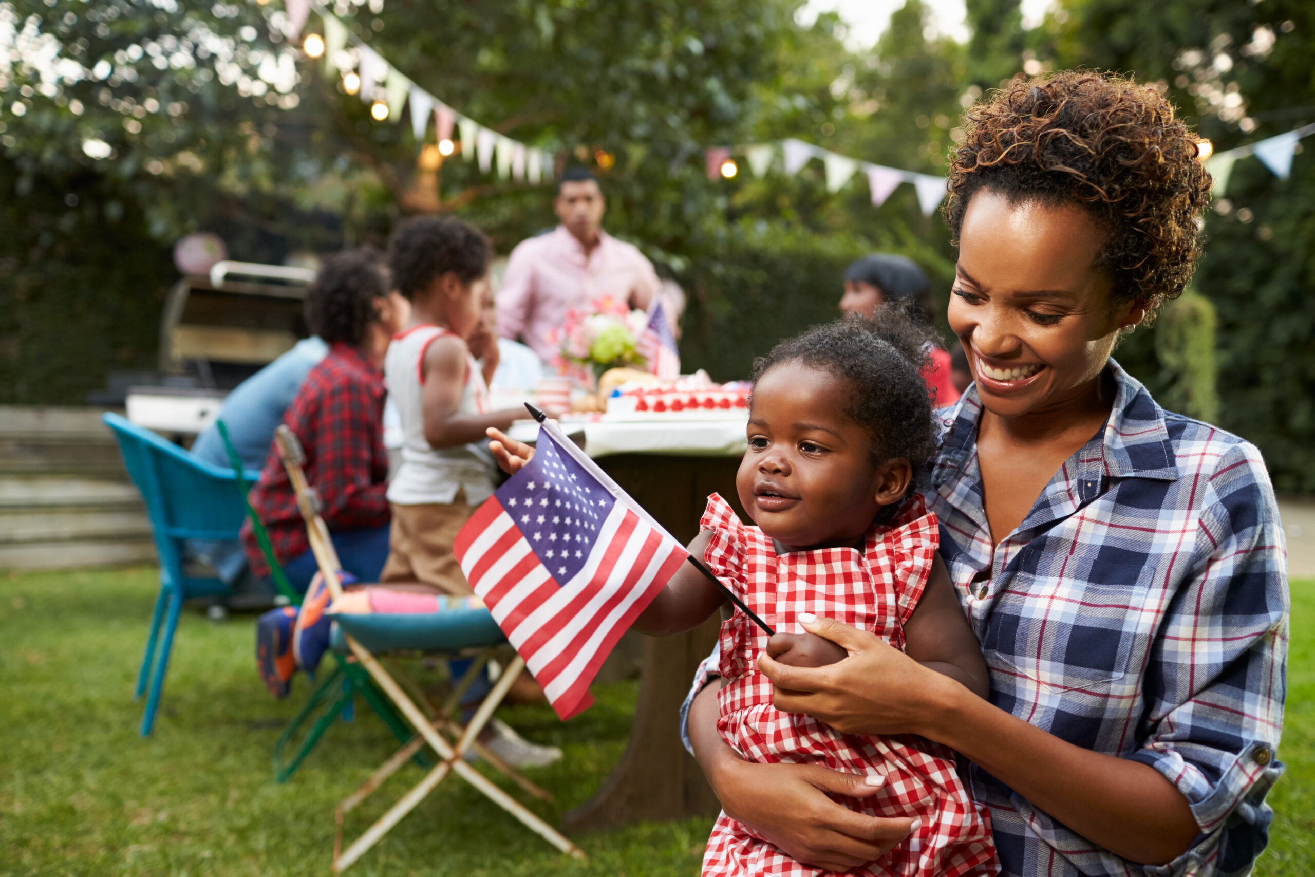 Black mother and baby holding flag at 4th July family picnic